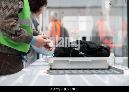 Baviera, Germania - 25 novembre 2025: Il bagaglio a mano è sottoposto a controlli di sicurezza obbligatori in aeroporto. Il personale controlla il processo mentre i sacchetti vengono scansionati sul nastro trasportatore per escludere gli oggetti pericolosi. Il giorno delle operazioni di prova per il nuovo gate del Terminal 1 dell'aeroporto di Monaco. *** Am Flughafen durchläuft das Handgepäck die obligatorische Sicherheitskontrolle. Personal überwacht den Ablauf, während Taschen auf dem Förderband durchleuchtet werden, um gefährliche Gegenstände auszuschließen. AM Tag des Probebetriebs für den neuen Flugsteig im Terminal 1 des Flughafens München. Foto Stock