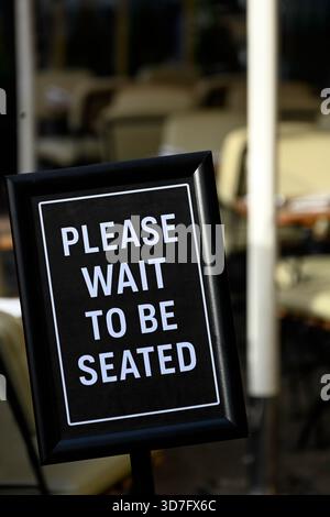 Aspetta di essere seduto con un cartello appeso sulla porta del ristorante Cafe Foto Stock