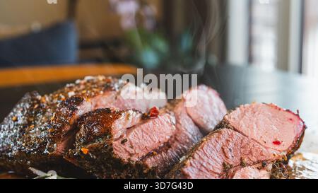 Arrosto di agnello disossato a fette su tavola di legno, incredibilmente succoso e succulento con erbe e rosmarino. Cucinato perfettamente, pronto a servire per specia Foto Stock