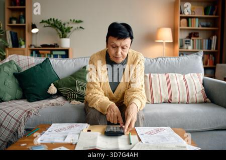 Donna anziana che esamina le fatture e calcola le fatture a casa Foto Stock