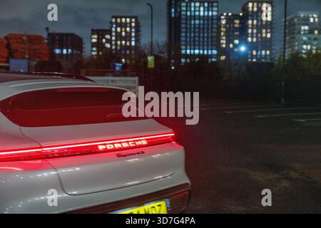 Parte posteriore di un'auto sportiva elettrica Porsche Taycan, che mette in risalto la caratteristica barra luminosa rossa a tutta larghezza con la scritta "Porsche" illuminata. Foto Stock