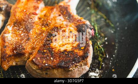 Cotolette di maiale sfrigolanti in una padella con aglio tostato intero e timo fresco. Marrone dorato, succoso e aromatico. Video di cottura perfetto per le ricette. Foto Stock
