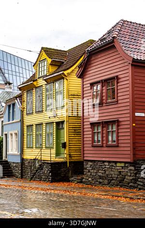 Case colorate in legno su una strada di Bergen con ciottoli bagnati e foglie autunnali cadute dopo la pioggia. Affascinante atmosfera autunnale, colori vivaci Foto Stock