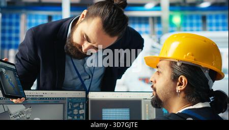 Il responsabile istruisce il dipendente dell'impianto di pannelli solari su come utilizzare il software CAD per ottimizzare i layout. Il supervisore della fabbrica fotovoltaica insegna ai lavoratori come predisporre la massima potenza, telecamera B. Foto Stock