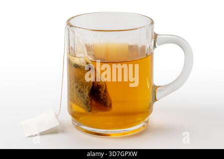 Rilassante tè digestivo alle erbe con camomilla e liquirizia in un sacchetto filtrante da immergere in acqua bollente in una tazza di vetro isolata su bianco con clippin Foto Stock