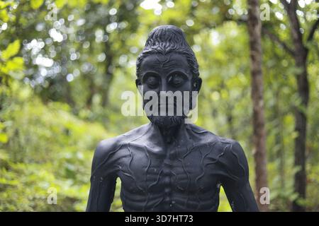 Tranquilla statua scura di un Buddha ascetico che meditava in una tranquilla foresta verde. la scultura pacifica rappresenta la spiritualità, la religione, l'illuminazione e. Foto Stock