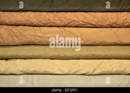 Rotoli stratificati di taffeta di seta spiegazzata in tonalità calde disposti su uno scaffale in un'officina sartoriale Foto Stock