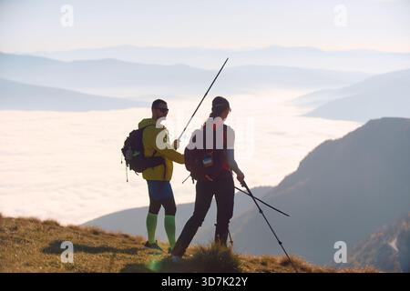 Due escursionisti godono di una spettacolare vista sulle montagne durante il trekking mattutino sopra un mare di nuvole Foto Stock