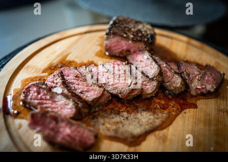 Primo piano, angolo basso di una bistecca di media rara affettata perfettamente su un tagliere di legno, guarnita con scaglie di sale marino grossolano e riposante nel suo guscio Foto Stock