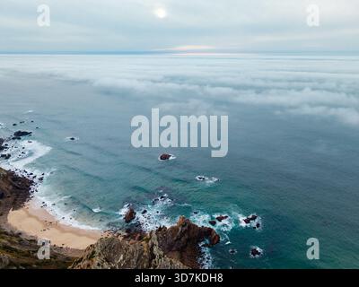 Splendida fotografia aerea che cattura una spiaggia di sabbia isolata e formazioni rocciose frastagliate lungo la costa di Cabo da Roca, Portogallo Foto Stock