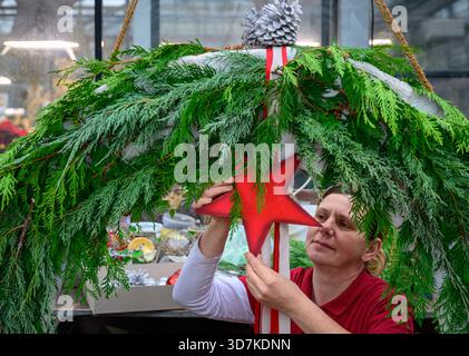 Lindenberg, Germania. 26 novembre 2025. Kathrin Herlein, fiorista di Gärtnerei Heinrich, crea una grande corona dell'Avvento. Il 30 novembre è il 1° Avvento. Ci sono molte interpretazioni diverse della corona dell'Avvento. Il simbolismo originale è l'aumento della luce come espressione della crescente attesa della nascita di Gesù Cristo. Crediti: Patrick Pleul/dpa/Alamy Live News Foto Stock