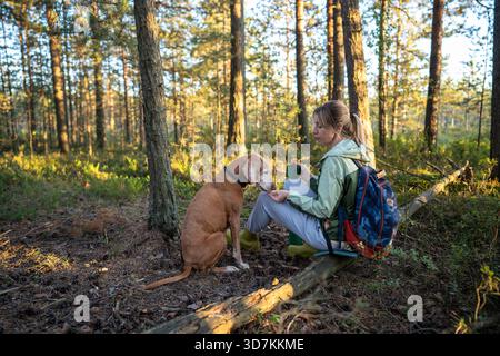 Una donna escursionista offre cibo per gli animali domestici che comunicano con calma sui sentieri boschivi. Accarezzamenti tra il proprietario e Vizsla, legame con gli animali in natura, nutrire il cane fedele, ricevere attenzioni per gli animali domestici a piedi || modello rilasciato Foto Stock
