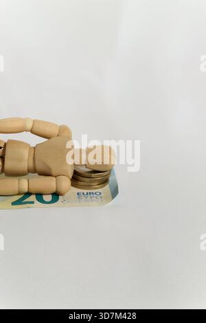 Manichino di legno che giace incline, schiacciato dal peso delle monete in euro e delle banconote Foto Stock