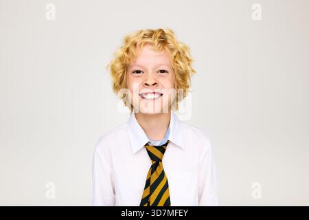 Allegro biondo in uniforme scolastica sorridente in un ambiente da studio. Foto Stock