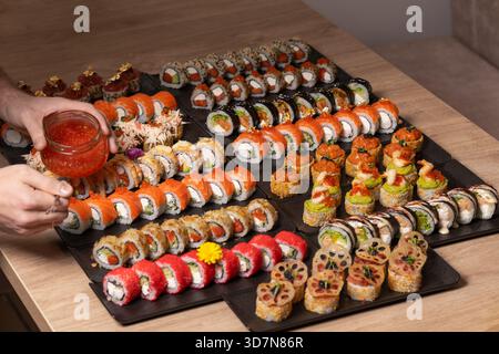 Una persona organizza un ampio piatto gourmet di vari tipi di sushi e maki, tra cui salmone, caviale rosso e condimenti elaborati, in un unico locale Foto Stock