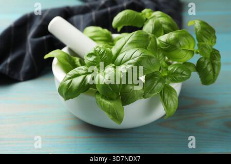 Mortaio con foglie di basilico fresco e pestello su un tavolo di legno azzurro, primo piano Foto Stock