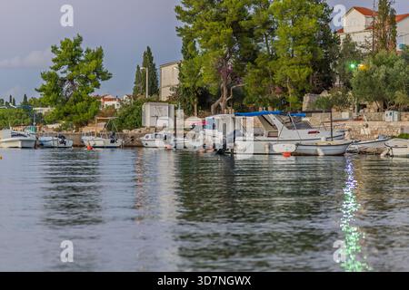 Un porto tranquillo con diverse barche attraccate lungo una costa verde. La luce del sole si riflette sull'acqua mentre alberi e case fiancheggiano la riva, trasportando lei Foto Stock