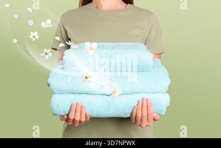 Donna che tiene in mano asciugamani freschi e piacevolmente profumati su sfondo verde chiaro, primo piano. Flussi di aroma e fiori dal bucato. Uso di ammorbidente per tessuti o Foto Stock