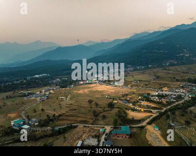 Vista aerea della luce del sole dorata che baciano i campi terrazzati mentre illumina la città annidata contro le maestose montagne tinto di blu, Baijnath e Himac Foto Stock