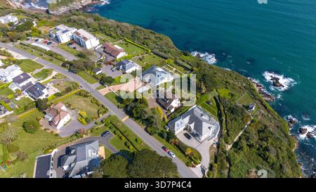 Vista aerea delle case annidate lungo la costa, il mare turchese che si schianta contro le verdeggianti scogliere, Carlyon Bay, Saint Austell, Regno Unito. Foto Stock