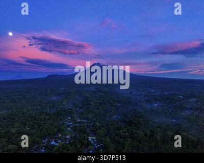 Vista aerea del maestoso Monte Merapi avvolto dalla nebbia mattutina, la sua vetta che pierge il cielo pastello sopra un mare della foresta di ​​green, Klaten Regency, CEN Foto Stock