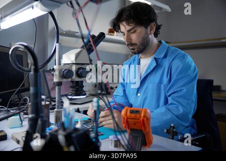 Il tecnico si è impegnato attivamente in lavori critici sulla scheda a circuiti stampati osservando al microscopio Foto Stock