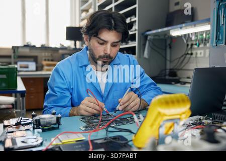 Un uomo che lavora con un cappotto blu si concentra sul lavoro con una scheda madre Foto Stock