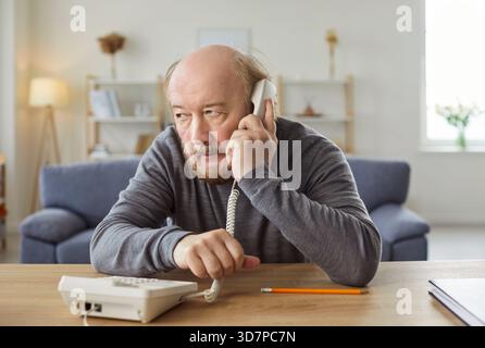 Uomo serio e maturo che parla, tiene il ricevitore vicino all'orecchio, effettua una chiamata telefonica Foto Stock