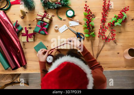 Le confezioni regalo per le feste sono appoggiate sul tavolo e i rotoli di carta rossa e verde sono situati nelle vicinanze Foto Stock