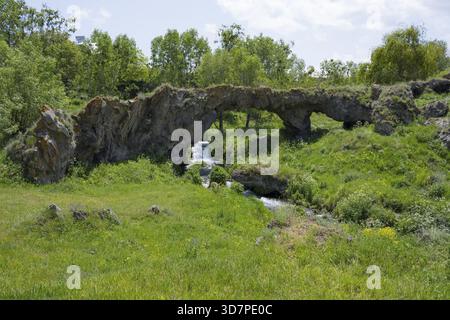 Scena con un arco di roccia naturale e una piccola cascata in un ambiente verde, il ponte Tsakkar nel villaggio di Tsakkar, provincia di Gegharkunik, Armenia Foto Stock
