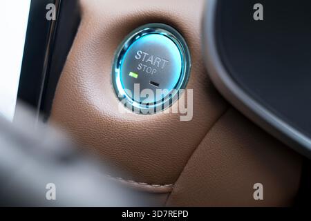Vista ravvicinata di un pulsante Stop/Start illuminato integrato in un cruscotto in pelle, che mette in risalto la moderna tecnologia di accensione e gli interni eleganti Foto Stock