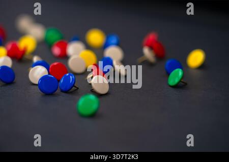 Una dispersione di miniature colorate (pulsanti) in rosso, blu, verde e beige su una superficie nera, con una profondità di campo bassa. Foto Stock