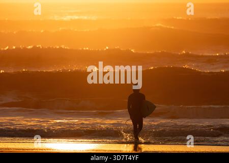 Surfista camminando sulla Ocean Beach al tramonto a San Francisco Foto Stock