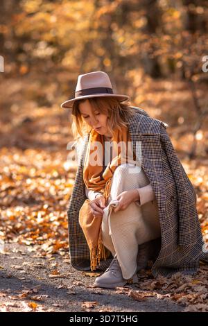 Donna Autumn Leaves Forest: Donna elegante in cappello piegato, esaminando le foglie autunnali sul terreno della foresta durante l'autunno. Foto Stock