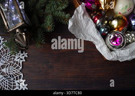 Composizione natalizia con ornamenti in vetro vintage, rami di pino, lanterna e fiocco di neve all'uncinetto fatto a mano su sfondo di legno scuro. Foto Stock