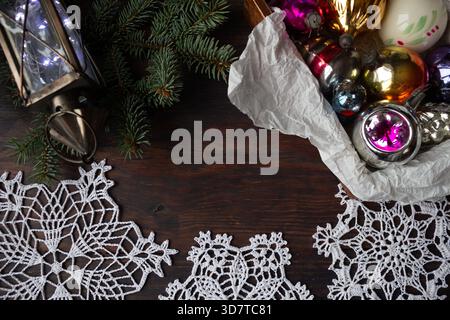 Composizione natalizia con ornamenti in vetro vintage, rami di pino, lanterna e fiocco di neve all'uncinetto fatto a mano su sfondo di legno scuro. Foto Stock