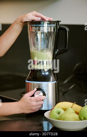 Giovane donna caucasica che mescola il frullato verde in cucina durante la mattina Foto Stock