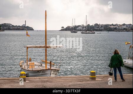 Donna in piedi con una barca a vela sul lungomare di Portocolom Foto Stock