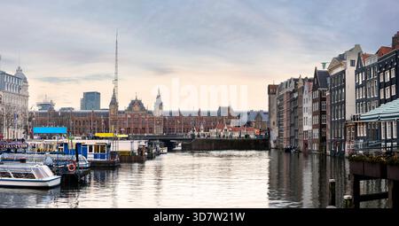 Crepuscolo al porto della stazione centrale di Amsterdam, con barche sui canali che scivolano sull'acqua, architettura storica e riflessi scintillanti durante la serata Foto Stock