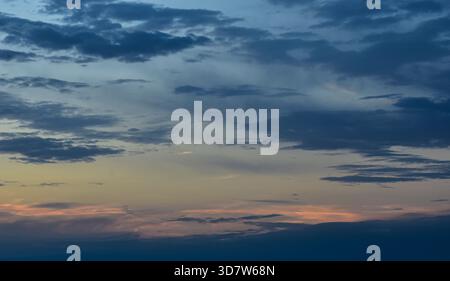 La luminosità del tramonto riempie il cielo di tonalità calde, illuminando delicatamente le nuvole e creando un momento sereno di tranquilla bellezza pomeridiana. Foto Stock