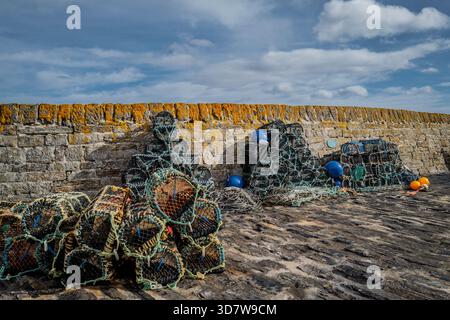 Pile di vasi di aragosta e boe colorate su un pavimento in pietra contro un muro di pietra intemprato. Porto di Keiss, Scozia Foto Stock