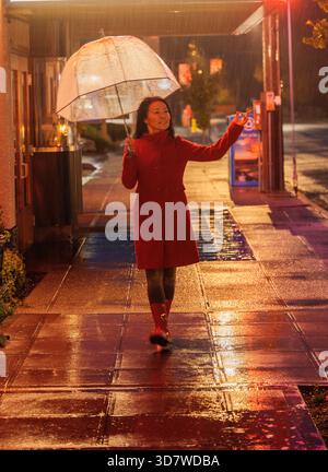 Donna con cappotto rosso che regge un ombrello trasparente su una strada piovosa. WASHINGTON, STATI UNITI Foto Stock