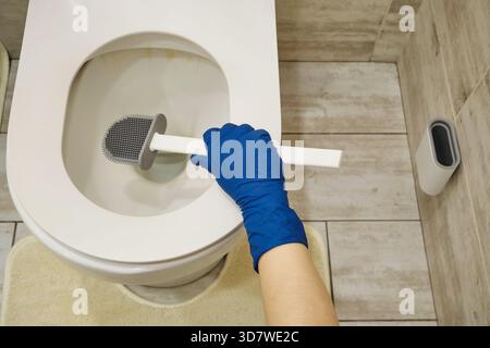 Indossare un guanto protettivo per pulire un WC sporco con una spazzola in silicone Foto Stock