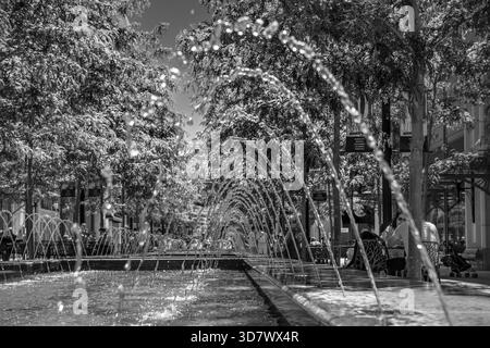 Fotografia in bianco e nero di fontane ad arco che creano un effetto tunnel nella piazza urbana con passerella alberata, Salt Lake City, Utah Foto Stock