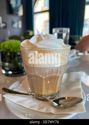 Elegante bicchiere di caffè a strati condito con panna montata in un elegante ambiente da caffe'. Stili di vita, cibo e ospitalità. Foto Stock