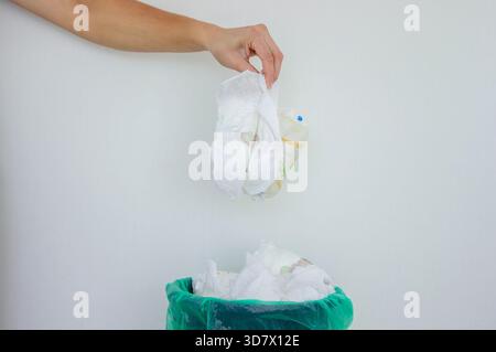 La mano di una donna che getta un pannolino usato in un cestino con una fodera verde. Foto Stock