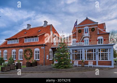 Un hotel in mattoni rossi con un'estensione blu, un albero di Natale festivo davanti, ghirlande e decorazioni stagionali che creano un caldo ambiente di vacanza. Foto Stock