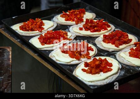 Focaccine fresche disposte su un vassoio, ognuna ricoperta di salsa cremosa e condita con pomodori tritati o paprika in un mercato di Street food natalizio. Foto Stock