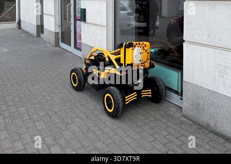Auto elettrica per bambini gialla e nera parcheggiata da un negozio con una simpatica valigia con motivi giraffe attaccata. Foto Stock