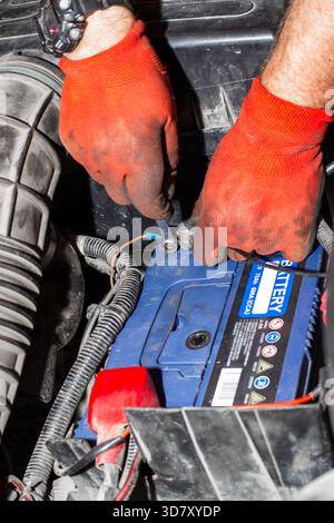 Durante la manutenzione o la riparazione, le mani con i guanti collegano e scollegano i morsetti della batteria di un veicolo sotto il cofano. Foto Stock